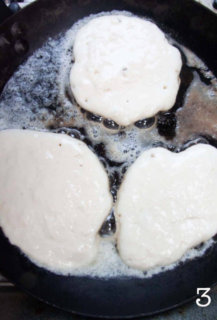 Three uncooked pancakes in a cast iron skillet.
