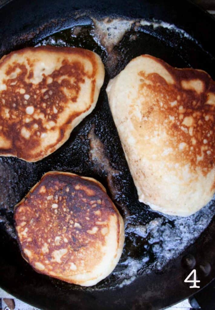 Three cooked pancakes in a cast iron skillet.