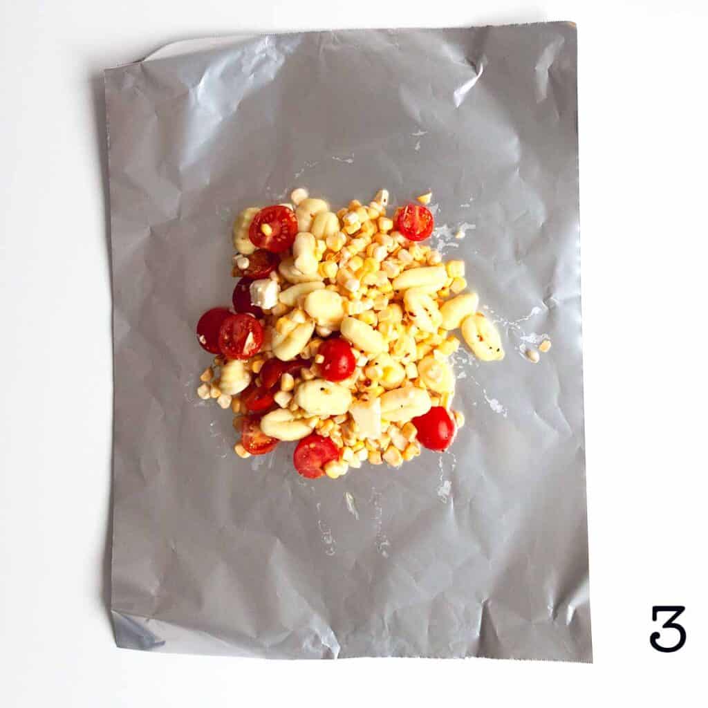 A mixture of corn, gnocchi, tomatoes, and corn on a sheet of aluminum foil.