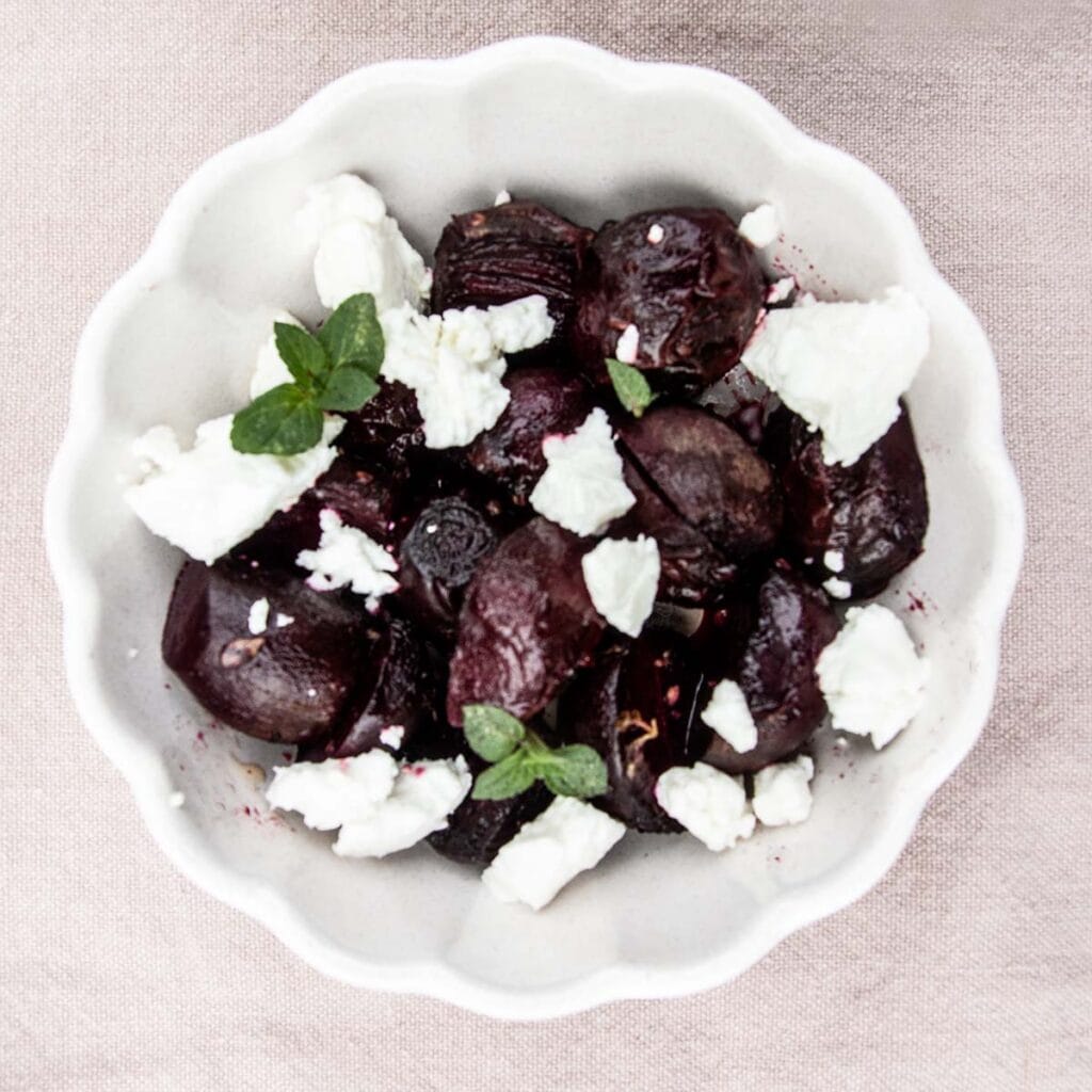 A white dish containing grilled beets topped with goat cheese and fresh mint.