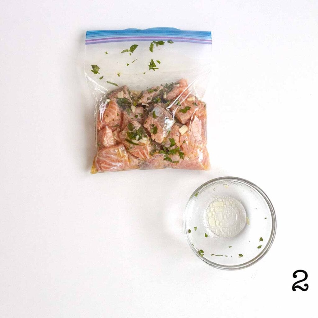 Cubed pieces of salmon in a zip-top bag with marinade and an empty bowl nearby.