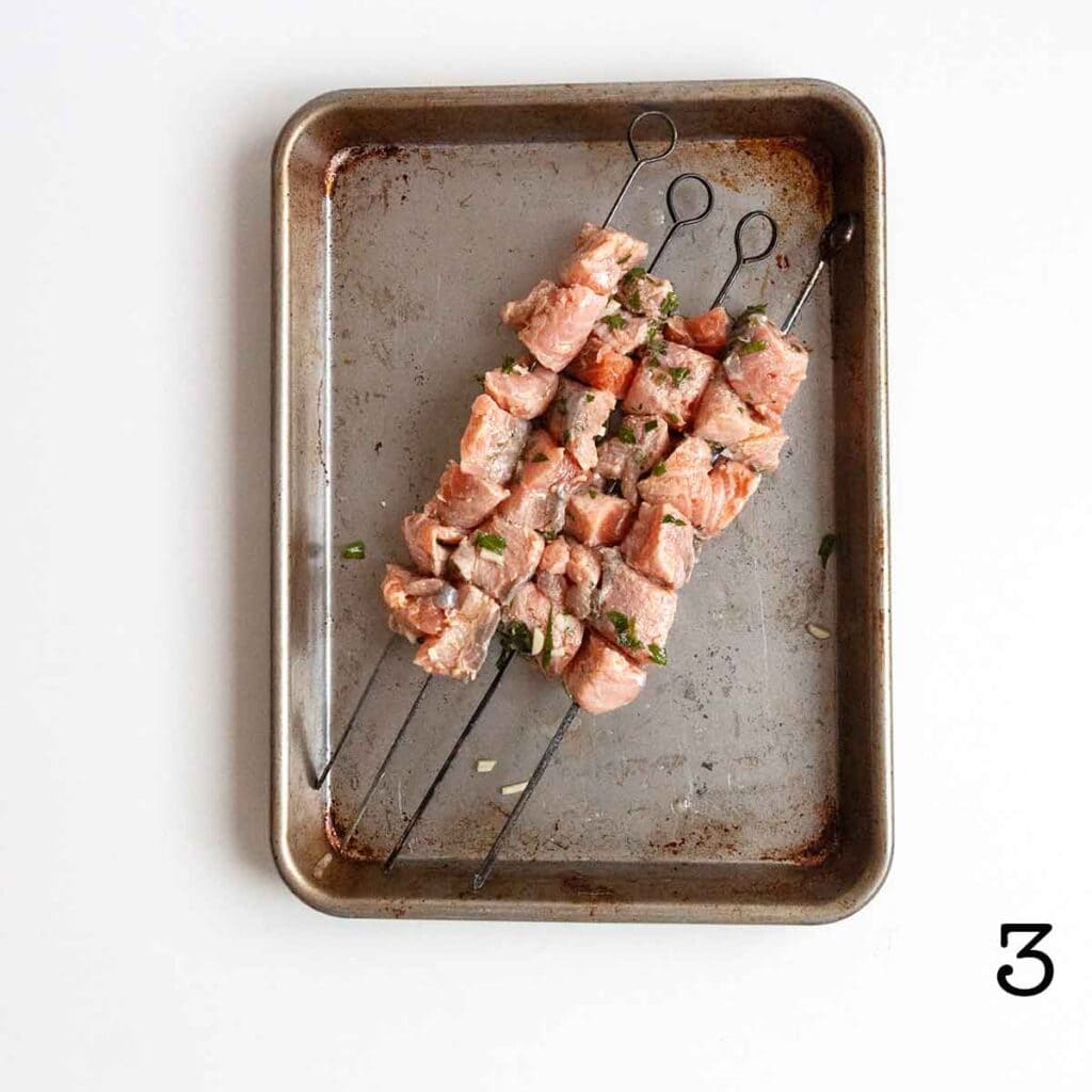 Four salmon kebabs on a rimmed baking sheet.
