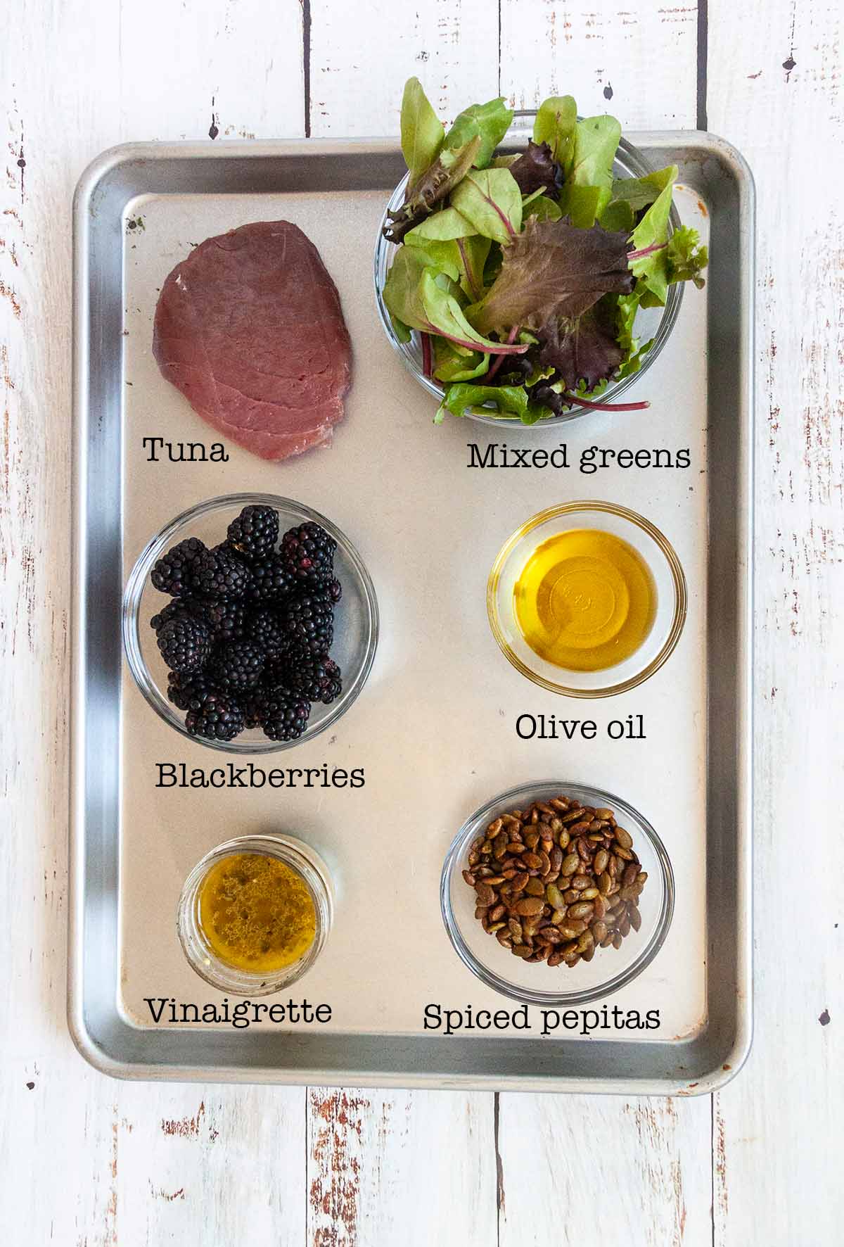 Ingredients for grilled tuna salad--tuna, greens, blackberries, olive oil, vinaigrette dressing, and spiced pepitas.