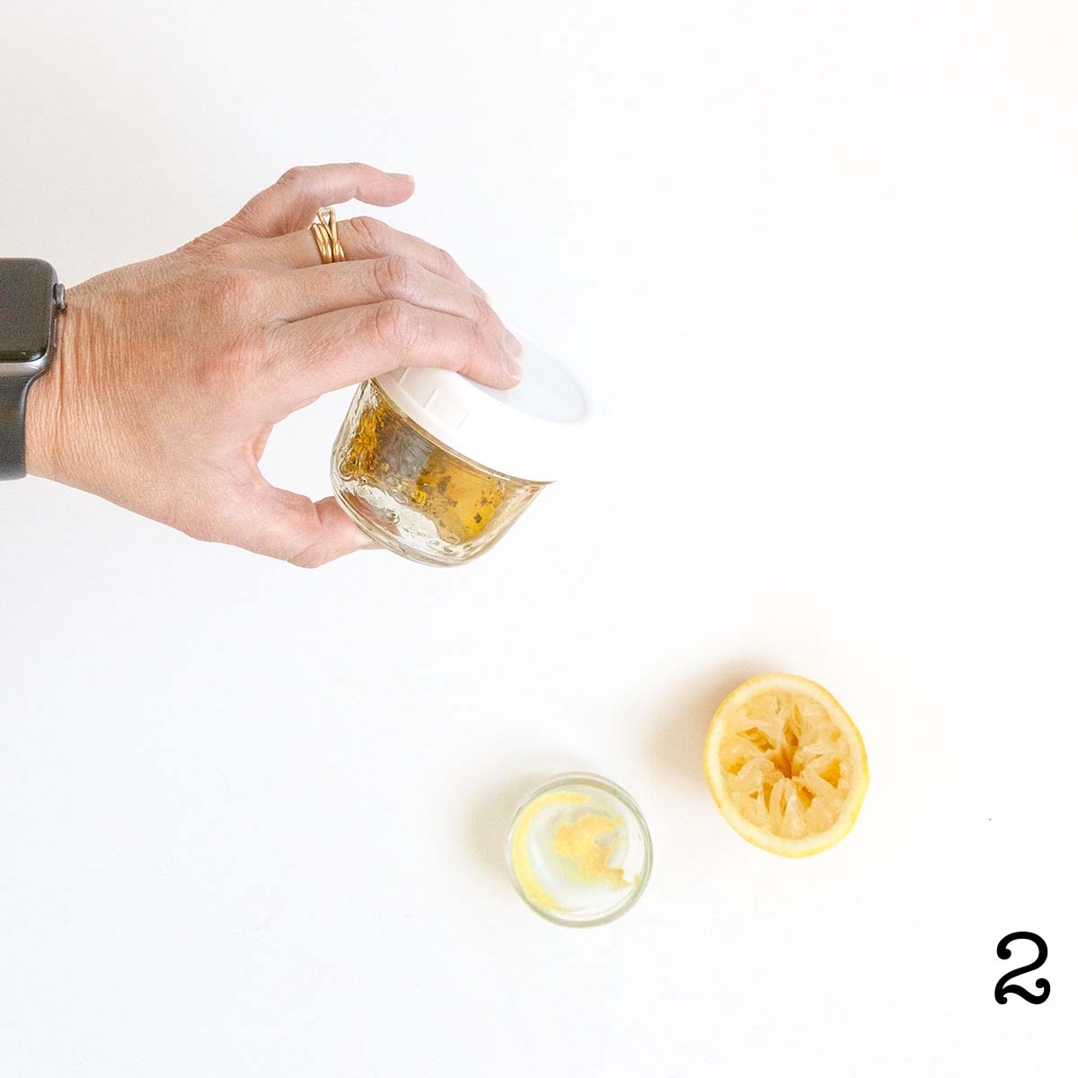 A person shaking up a jar of lemon thyme vinaigrette next to a squeeze half lemon and an empty dish of Dijon mustard.