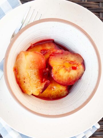 Spiced grilled plums in a bowl on a plate with a fork and checkered napkin on the side.