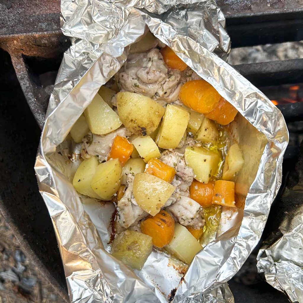 Chicken, carrots, and potatoes in bite size pieces in a foil packet over the fire.