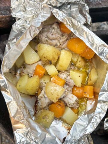 Chicken, carrots, and potatoes in bite size pieces in a foil packet over the fire.
