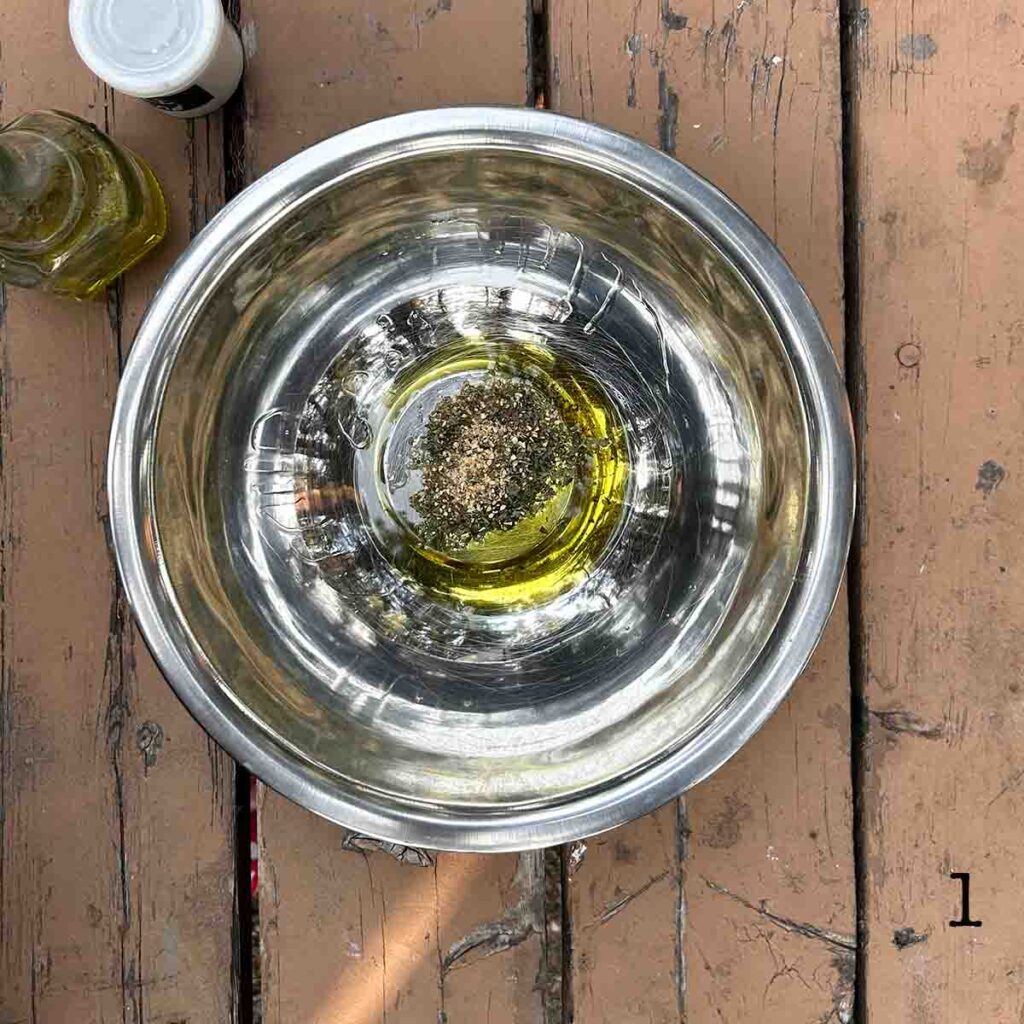 A metal bowl with olive oil and seasoning in it.