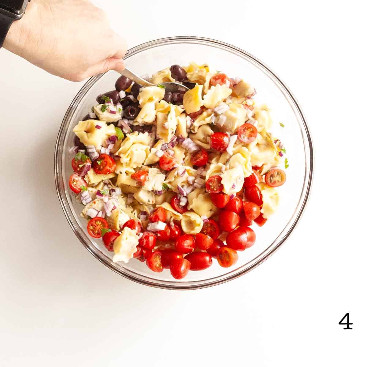 A person stirring a bowl of tortellini salad.