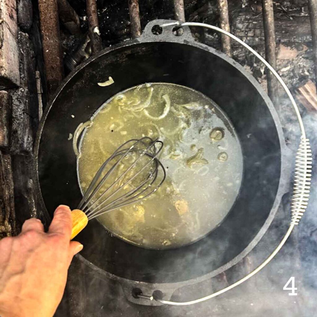 A person stirring broth and onions in a Dutch oven over a fire.