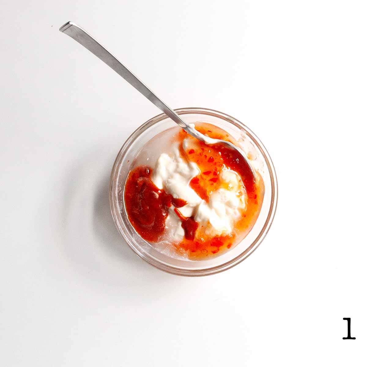 Several sauces in a glass bowl with a spoon resting inside.