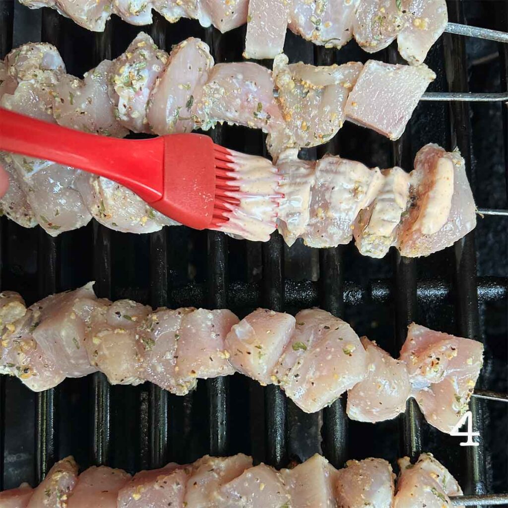 Chicken skewers on a grill being brushed with sauce.