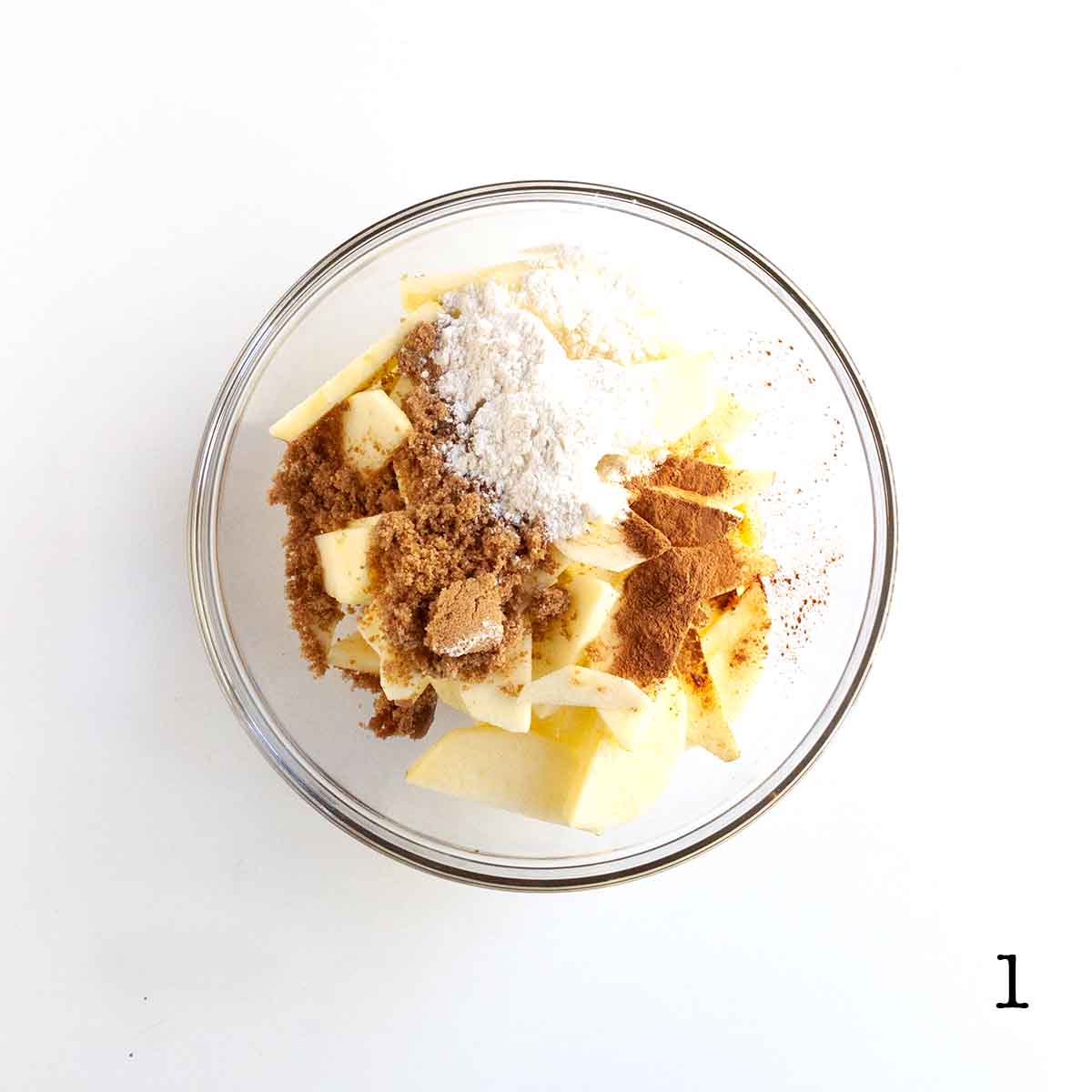 Apples, flour, brown sugar, and cinnamon in a glass bowl.