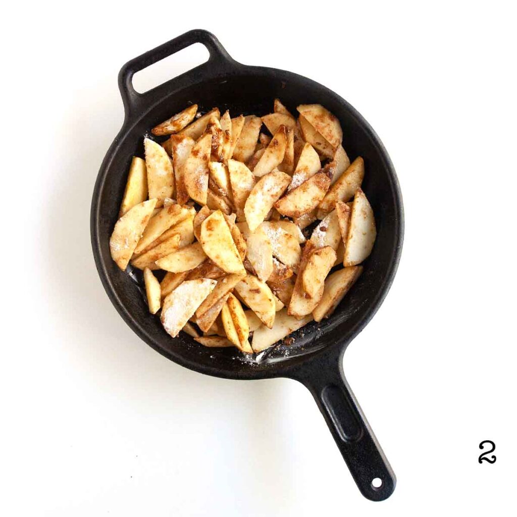 Apple slices coated with cinnamon and sugar in a cast iron skillet.