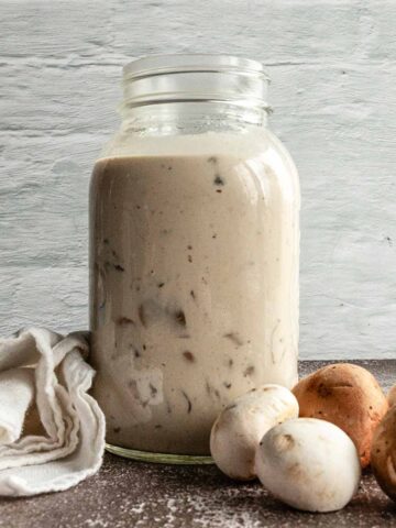 A jar filled with creamy mushroom sauce with some mushrooms next ot it.