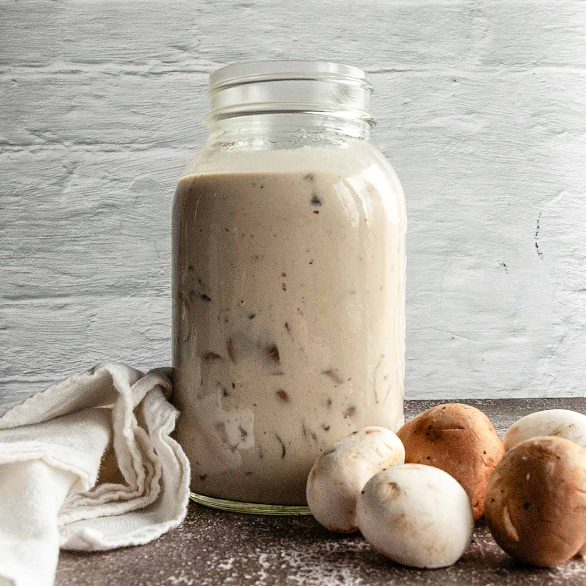 A jar filled with creamy mushroom sauce with some mushrooms next ot it.
