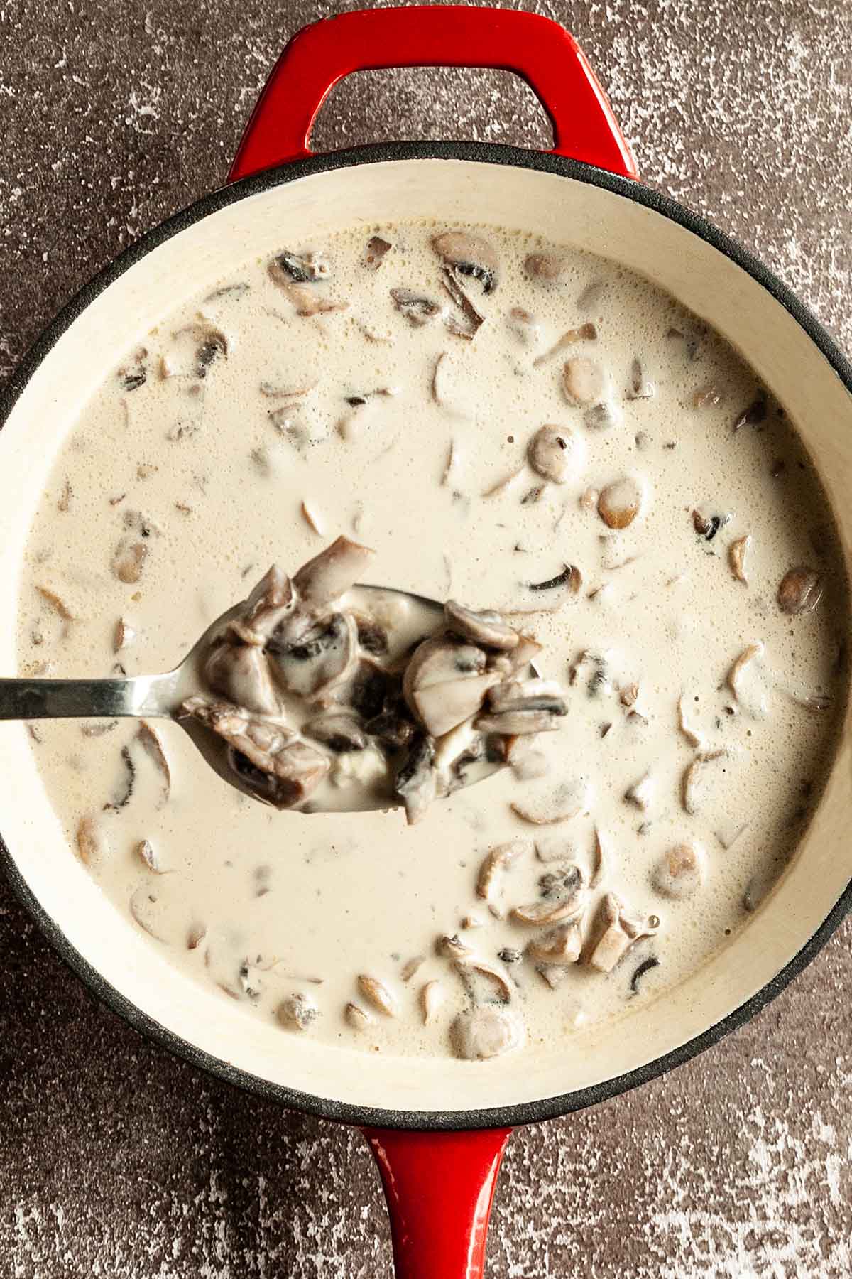 A spoonful of creamy mushroom sauce being lifted from a skillet.