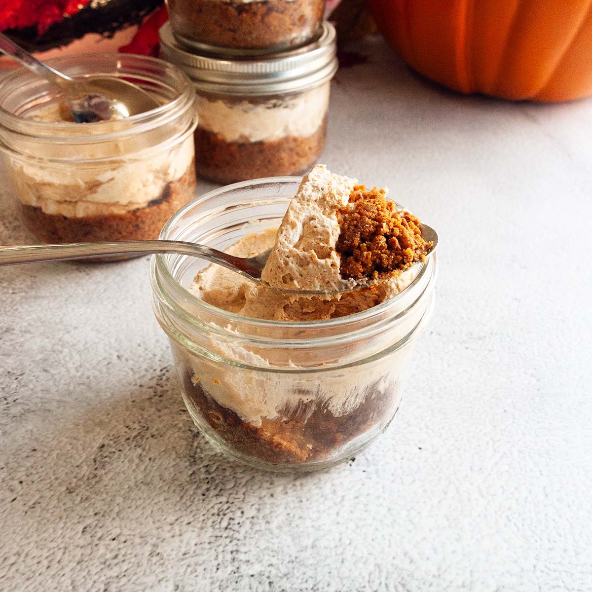 A spoonful of no-bake mini pumpkin cheesecake resting on top of a mason jar filled with the cheesecake.