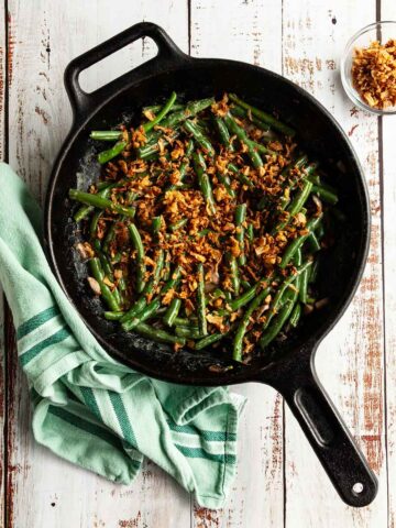 Green bean casserole in a cast iron skillet with fried onions on the side.