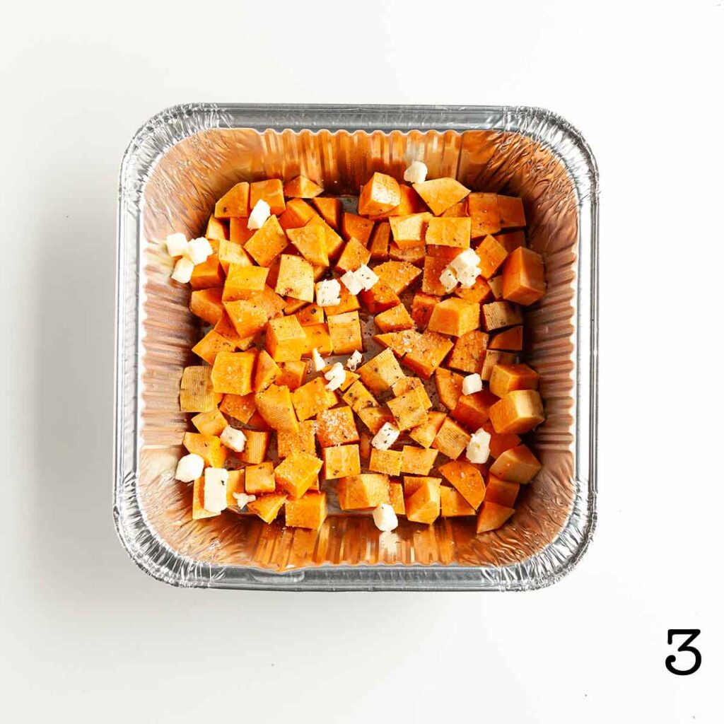 A foil tray filled with cubed sweet potatoes, topped with butter.