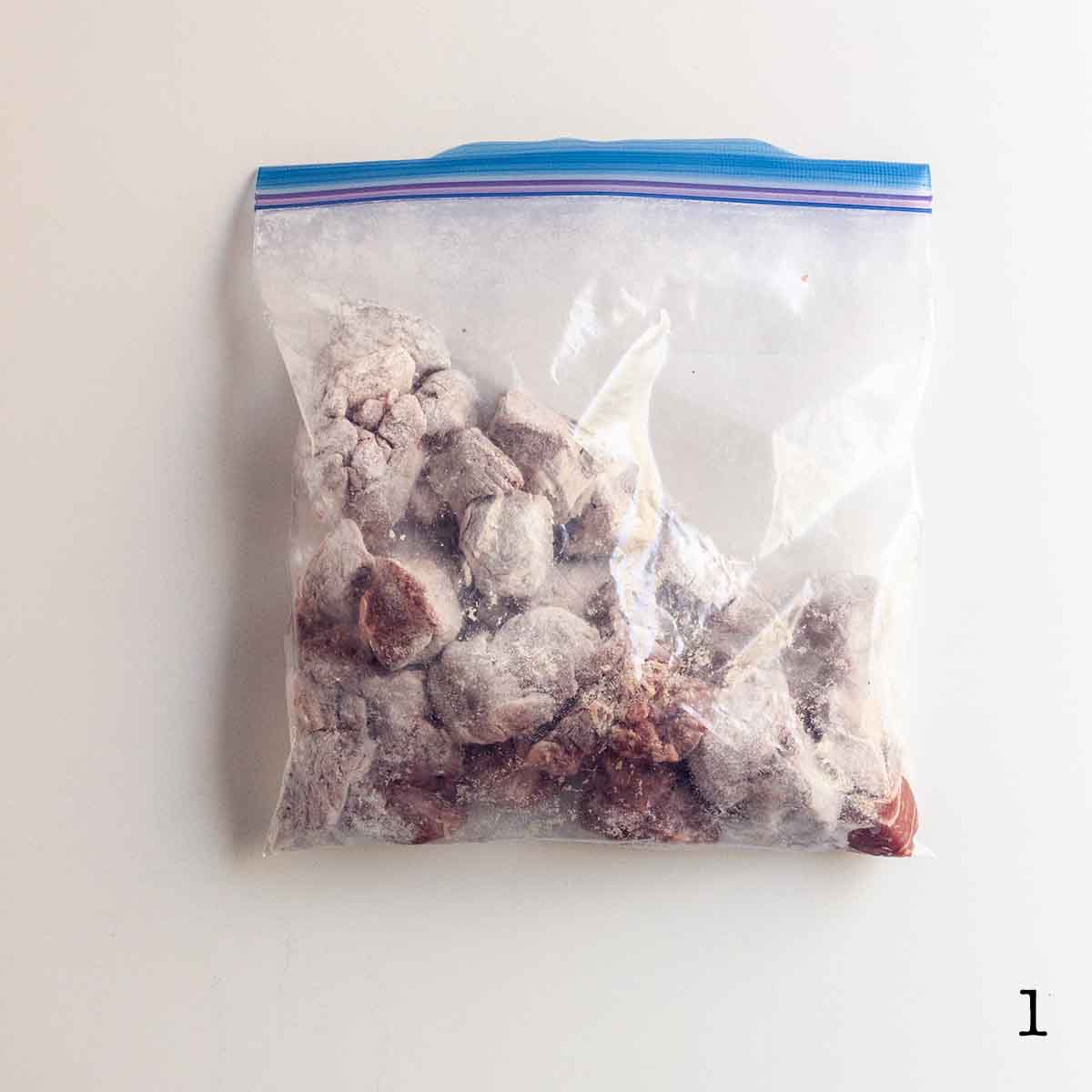 Cubes of stew meat coated in flour in a resealable plastic bag.
