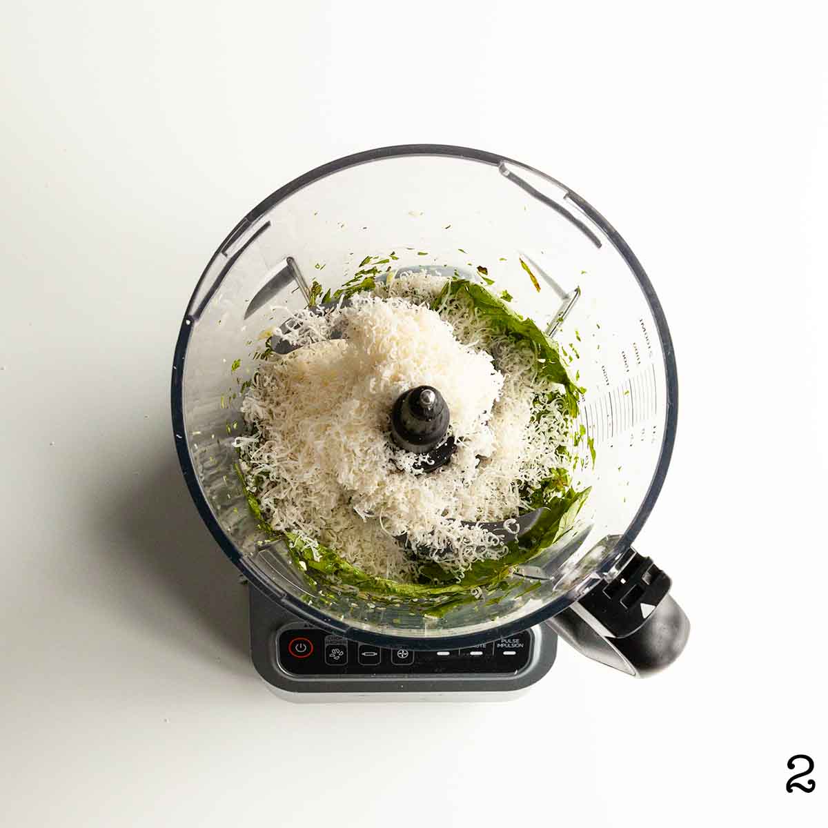 A food processor filled with chopped basil and Parmesan cheese.