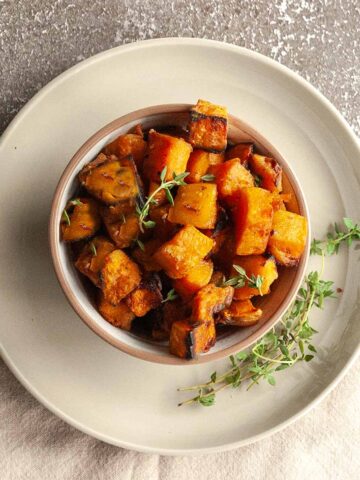 A bowl of cubed smoked sweet potatoes with crispy edges, with several thyme sprigs on the side.