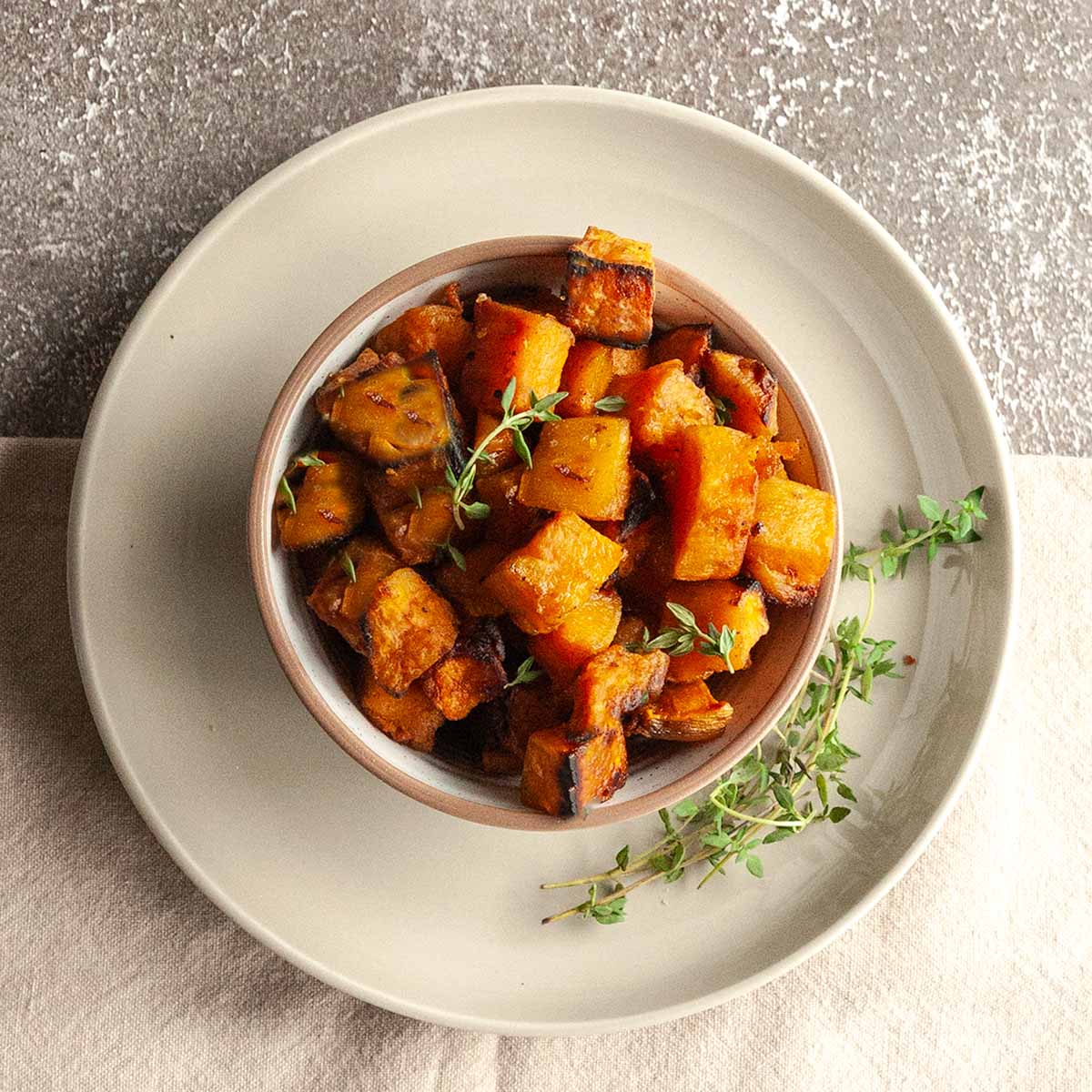 A bowl of cubed smoked sweet potatoes with crispy edges, with several thyme sprigs on the side.