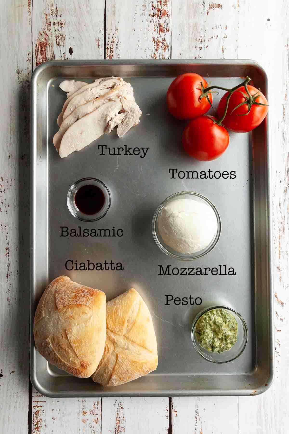 Ingredients for a turkey ciabatta sandwich--turkey, tomatoes, balsamic vinegar, mozzarella, ciabatta, pesto.