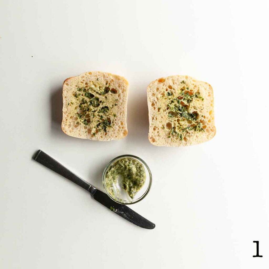 Pesto spread onto two cut halves of a ciabatta bun.