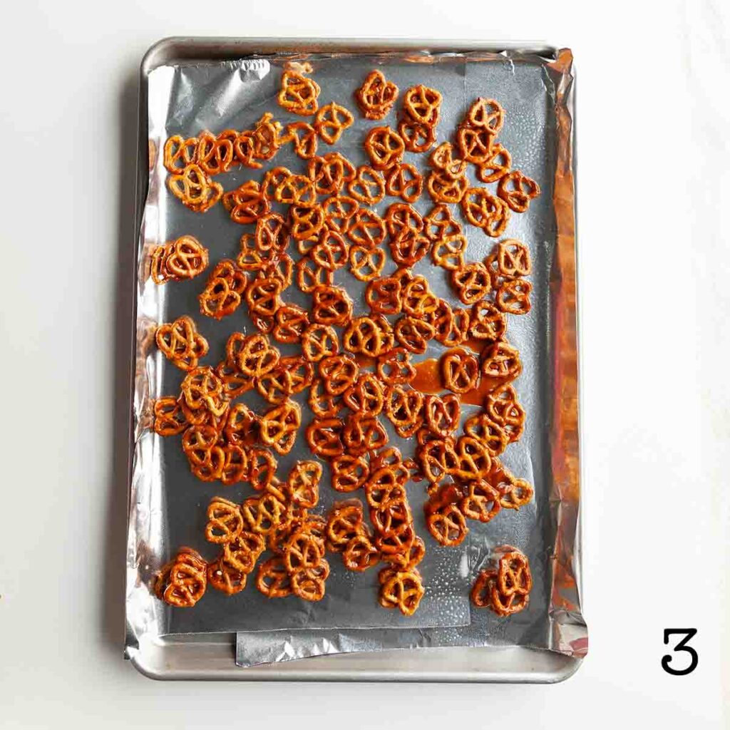 Toffee-coated pretzels arranged in a single layer on a foil-lined baking sheet.