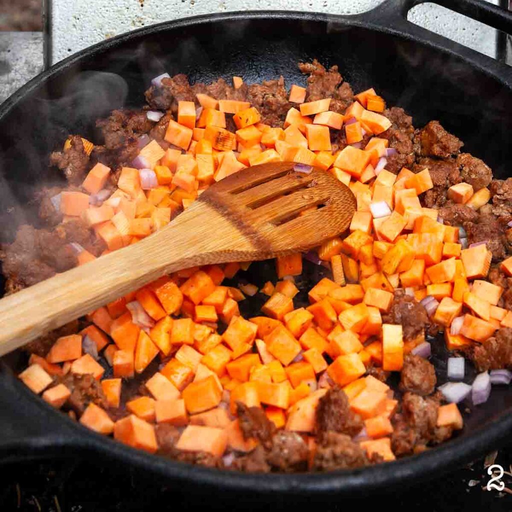 A skillet with chorizo, diced sweet potato, and red onion.