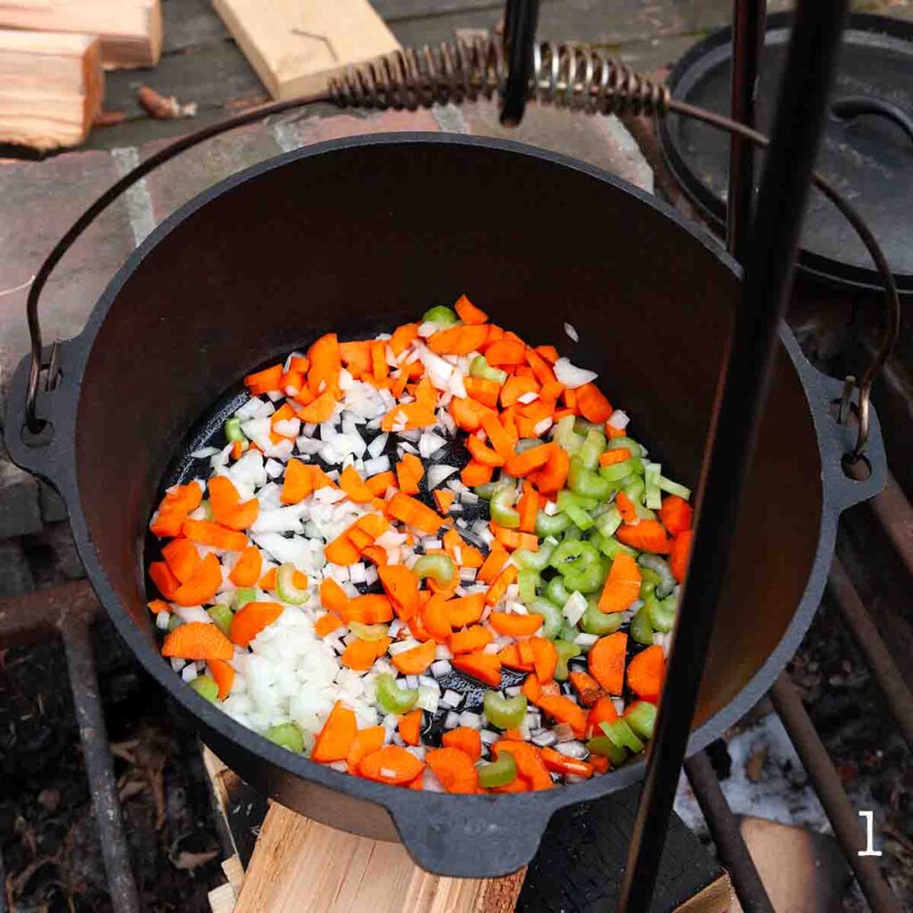 Celery, carrots, and onion in a Dutch oven over a fire.