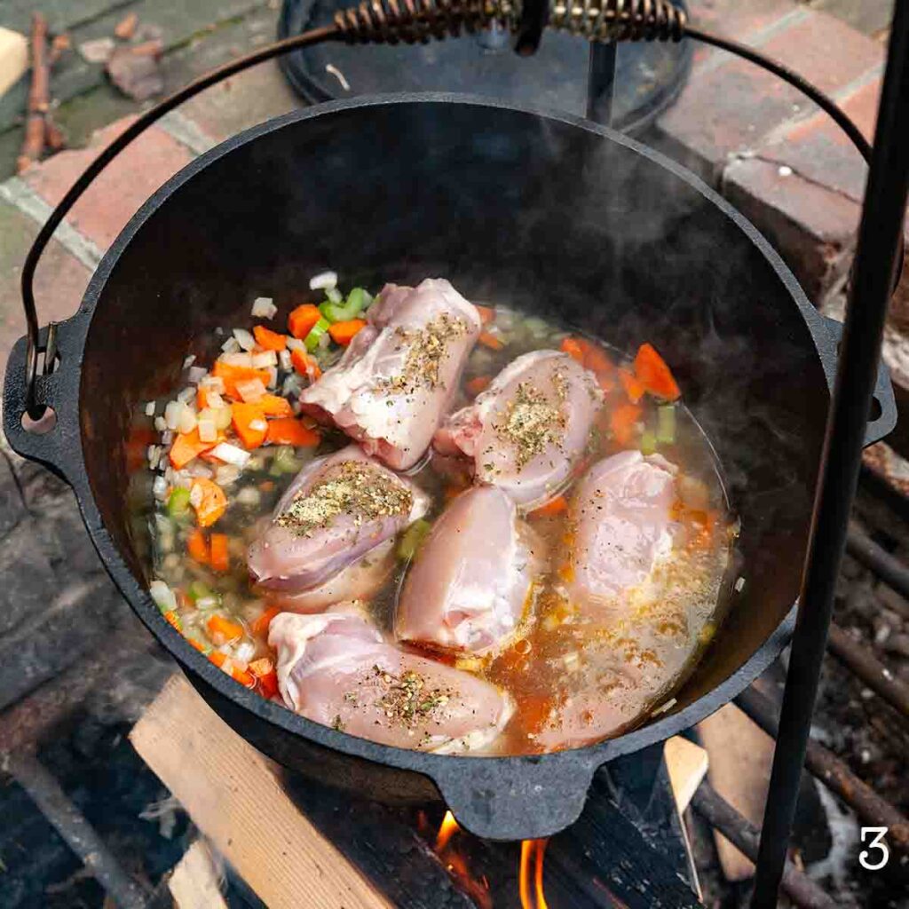 Chicken broth in a Dutch oven with sautéed vegetables and chicken thighs.