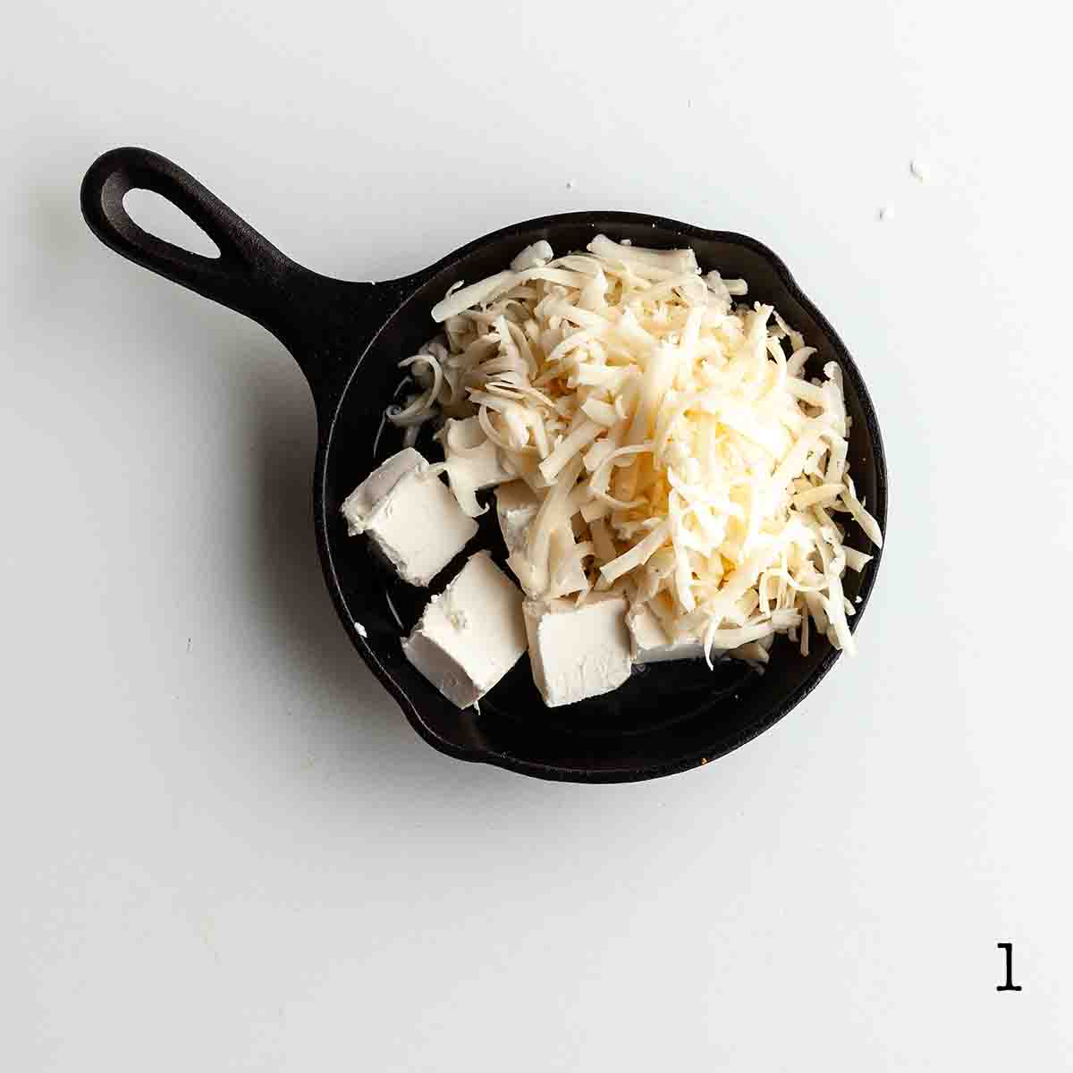 Cream cheese and grated Swiss cheese in a cast iron skillet.