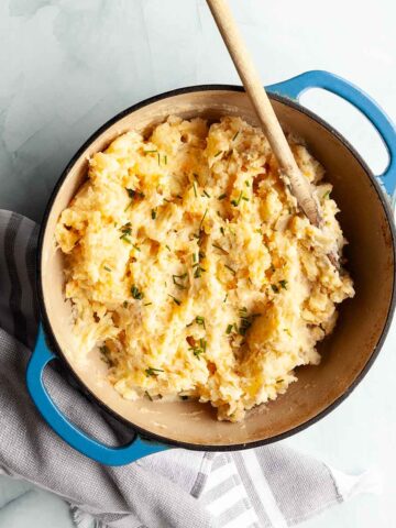 A pot of mashed potatoes with a wooden spoon resting inside.