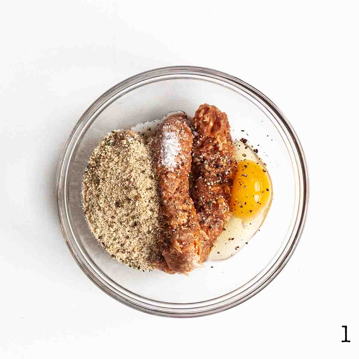Italian sausage, egg, and bread crumbs in a glass bowl.