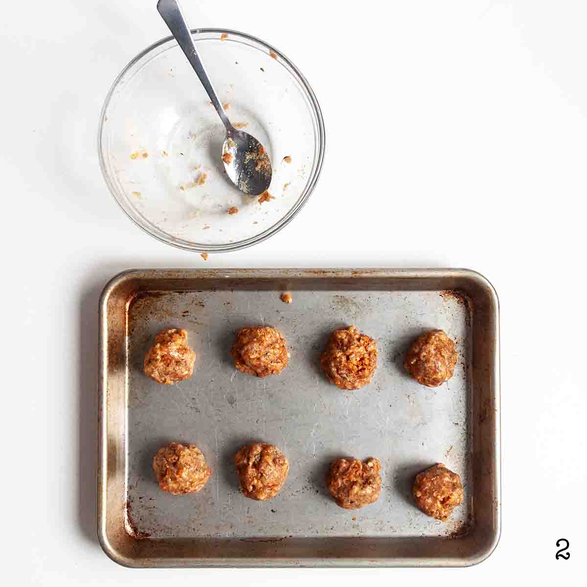 Eight Italian sausage slider balls with an empty mixing bowl nearby.