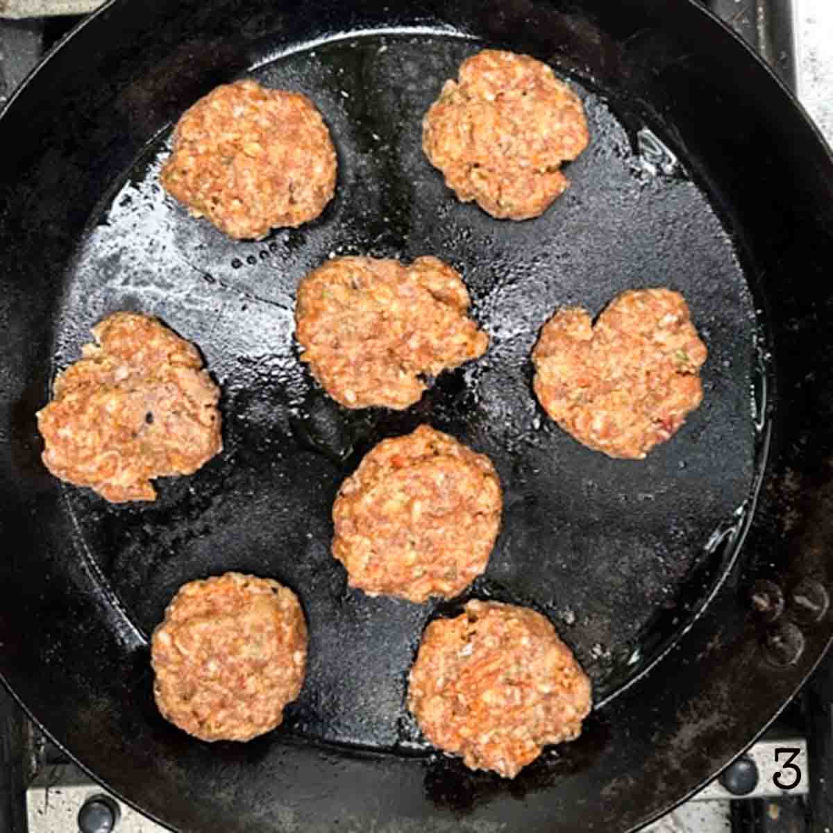 Eight Italian sausage slider patties in a skillet.