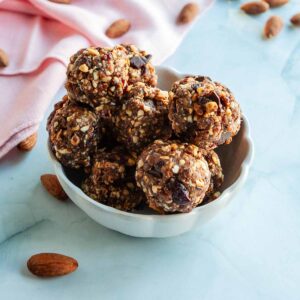 Several no-bake energy bites in a dish with almonds scattered around.