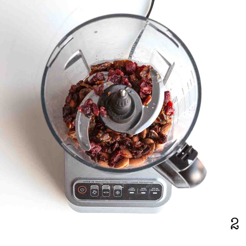 A food processor with dried fruit and nuts in it.