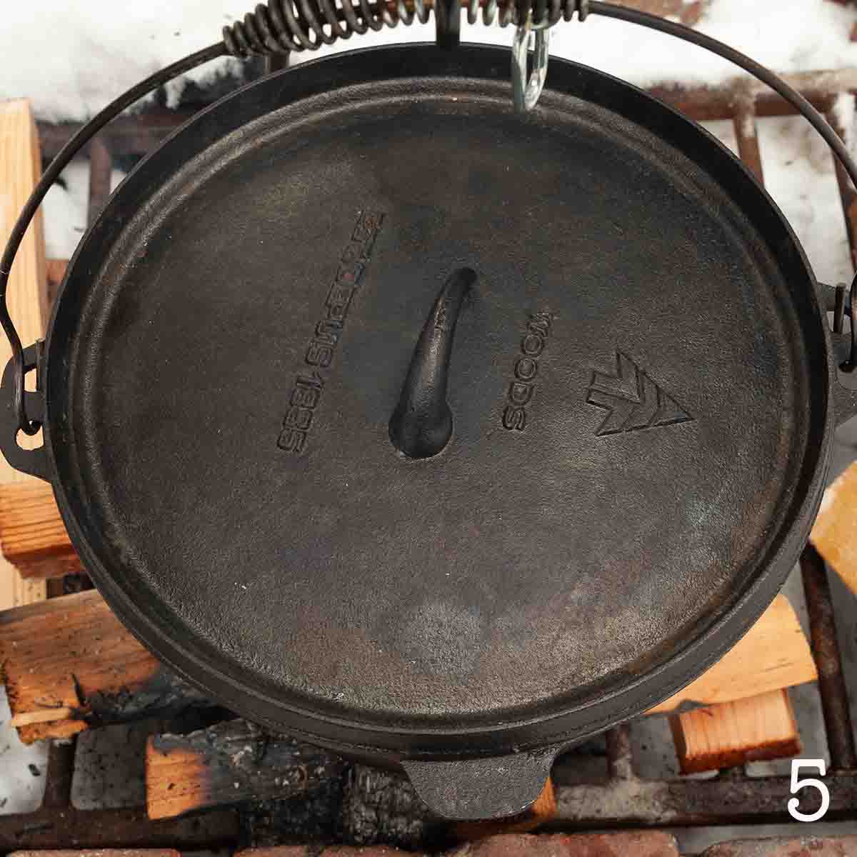 A covered Dutch oven over a campfire.