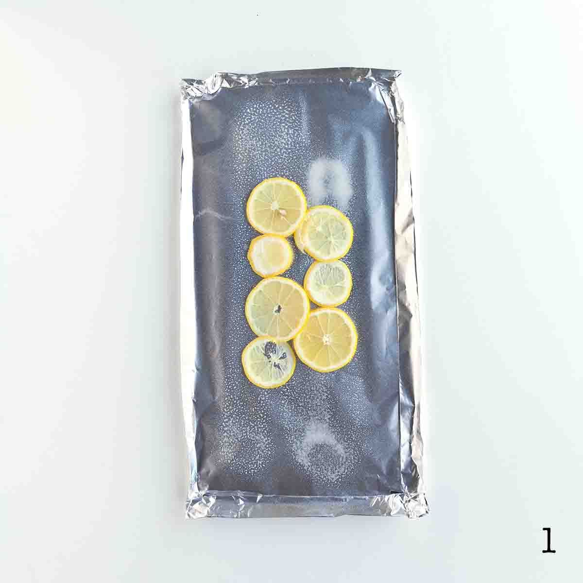 A sheet of foil with seven lemon slices arrange in a single layer.