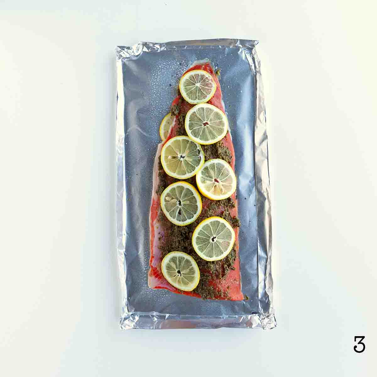 A fillet of salmon with pesto and lemon slices on top on a sheet of foil.