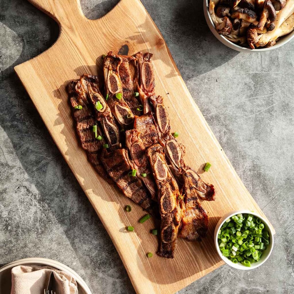 Strips of grilled flanken short ribs on a wooden board.
