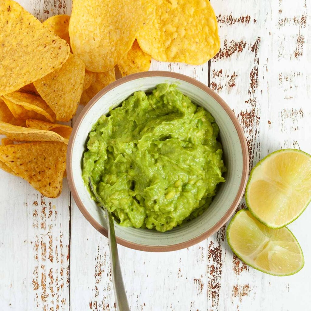 A bowl of guacamole with chips and lime wedges on the side.