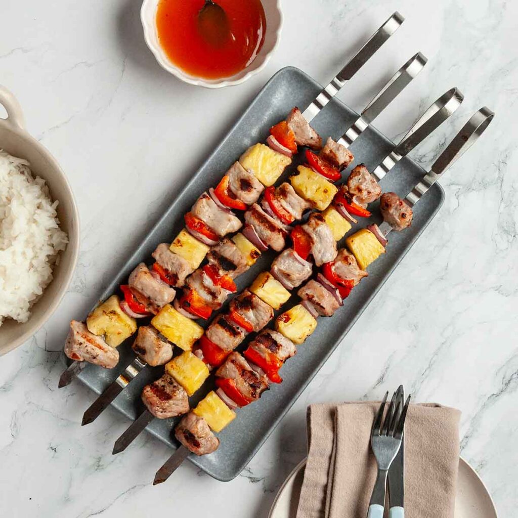 Four sweet and sour pork skewers with pork cubes, pineapple, pepper, and onion.