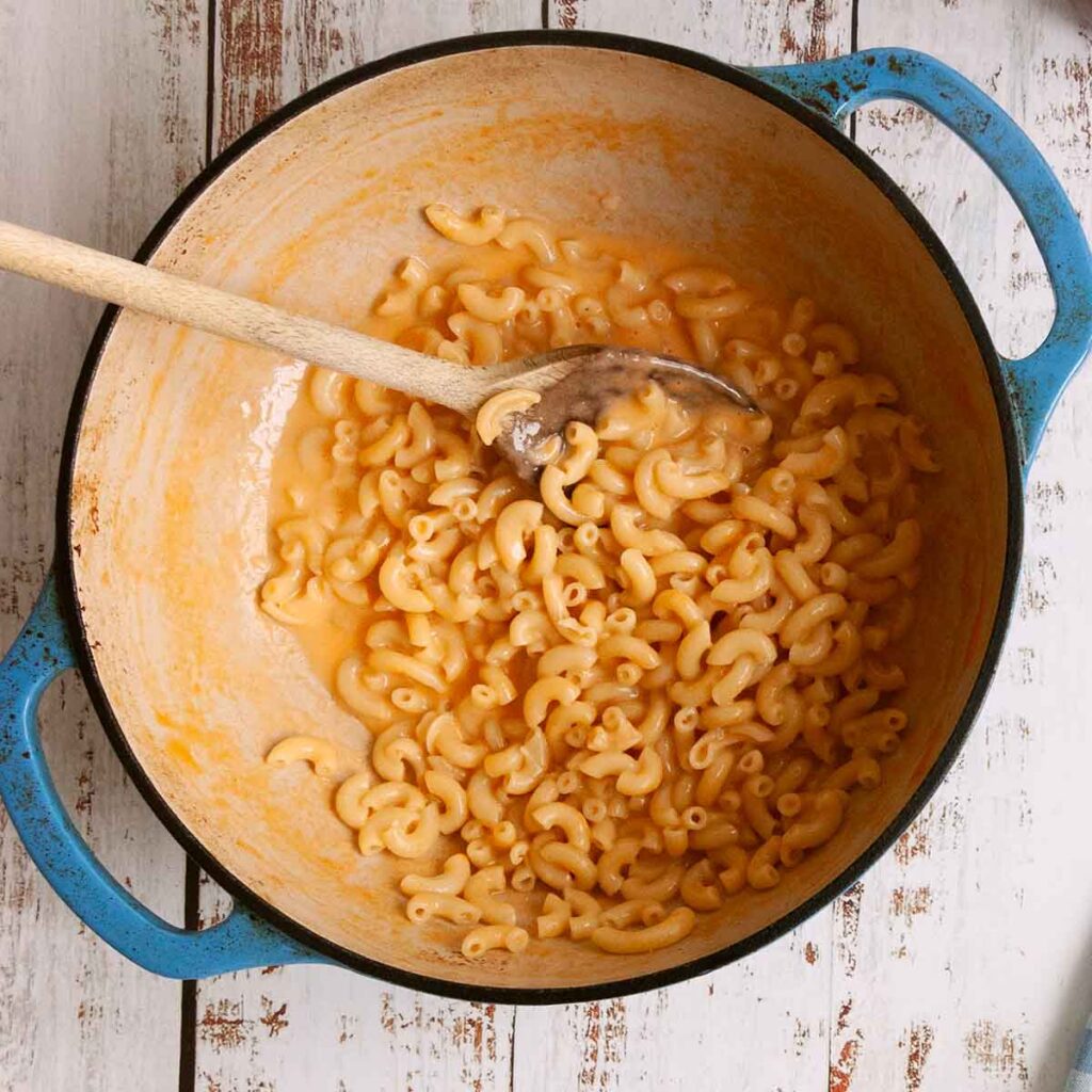 Creamy mac and cheese in a pot with a wooden spoon resting in it.