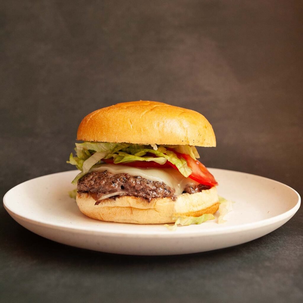 A burger with cheese, lettuce, and tomato on a plate.