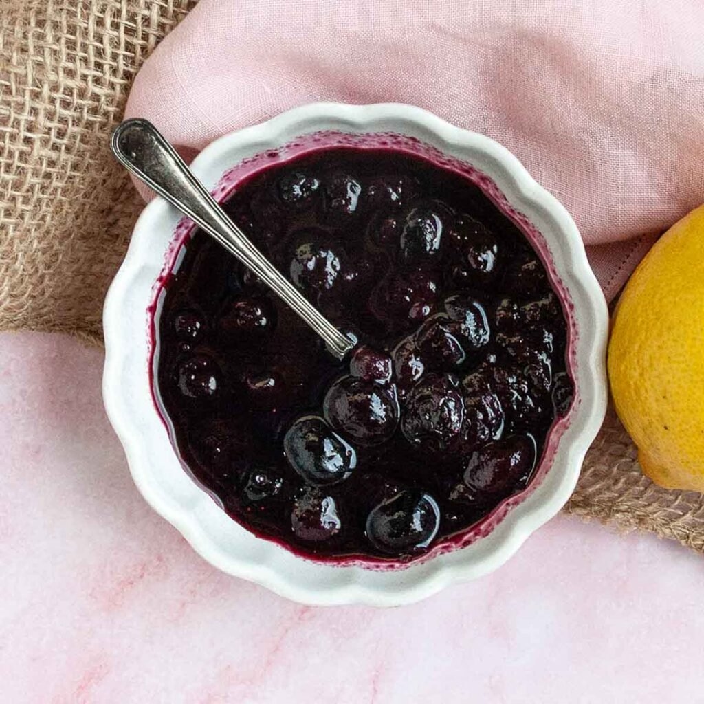 A dish of blueberry sauce with a spoon resting inside.